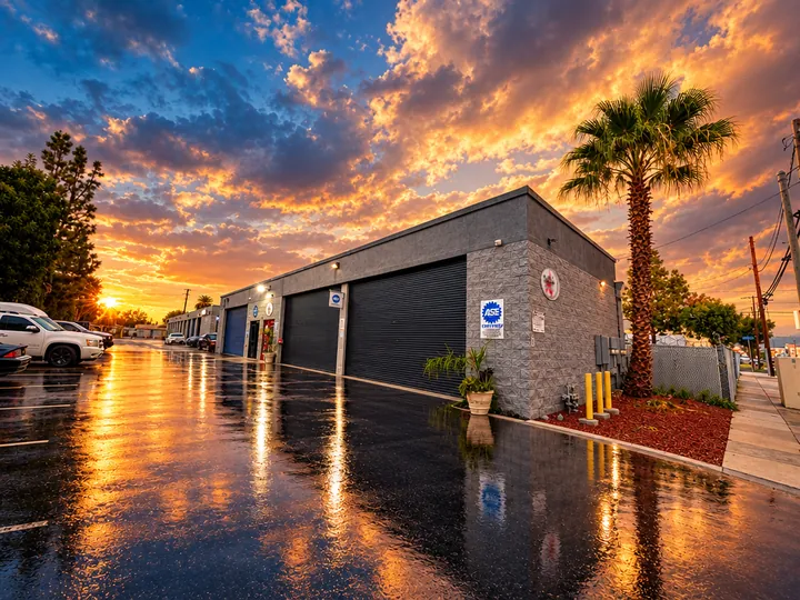 Cedillo's Classic & Auto Repair building in Fullerton with ASE sign and bay doors, wet pavement reflecting a stormy sunset
