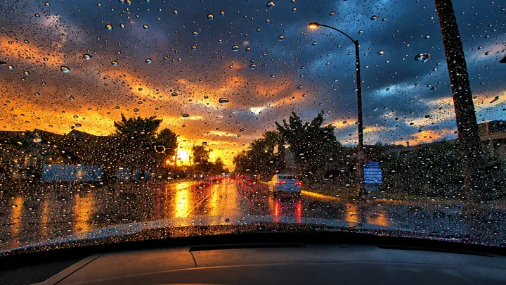 Heavy raindrops on a windshield at dusk on a Fullerton street, with oncoming headlights on wet pavement