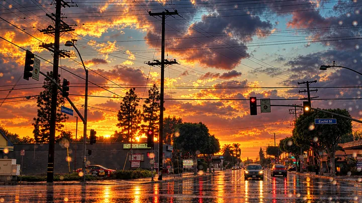 Rain-slicked intersection on Euclid St in Fullerton under a stormy sunset sky with traffic signals