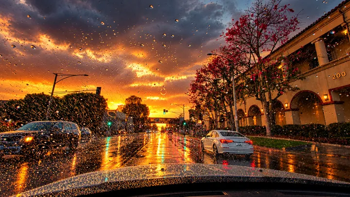 Rain on the windshield beside an arched building and a blooming tree on a wet Fullerton street