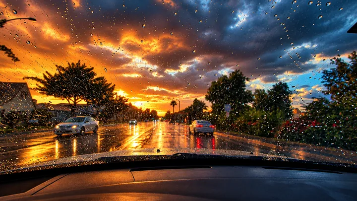 Raindrops on a windshield while driving a wet Fullerton street at sunset
