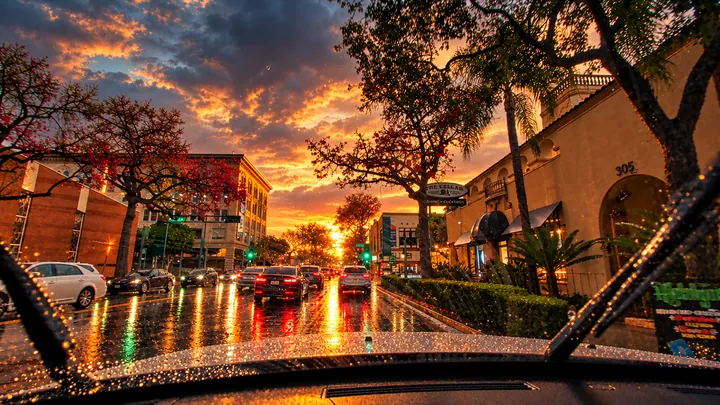 Rainy evening traffic past historic buildings in Fullerton, wet pavement reflecting brake lights